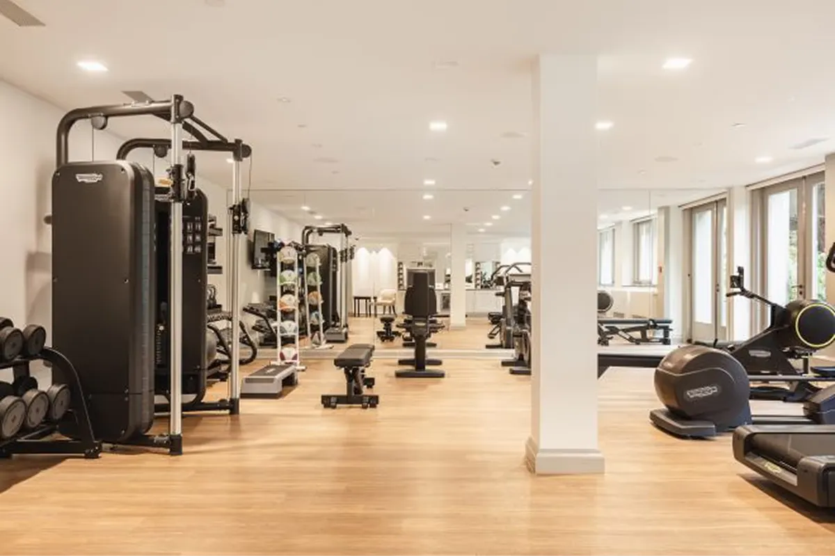 A gym with workout machines lined against wood-clad walls on light wood flooring in a bright space