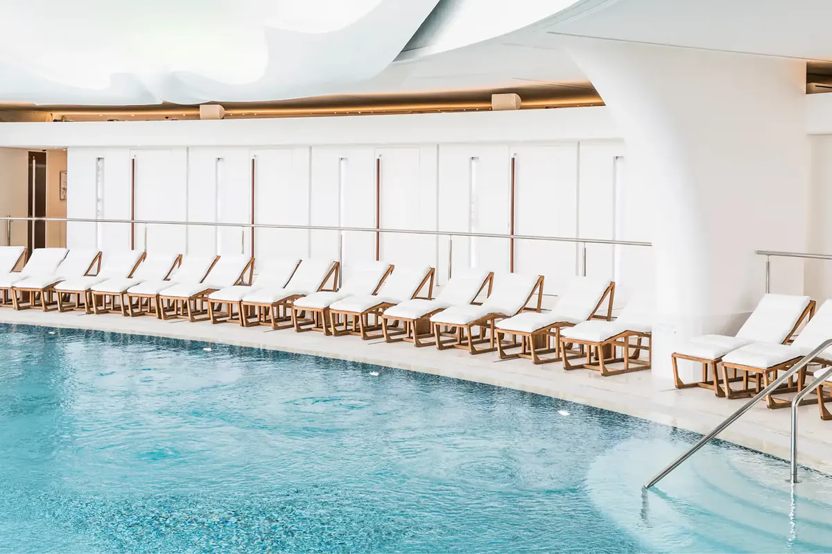 Indoor lap pool with floor-to-ceiling windows and parallel rows of lounge chairs