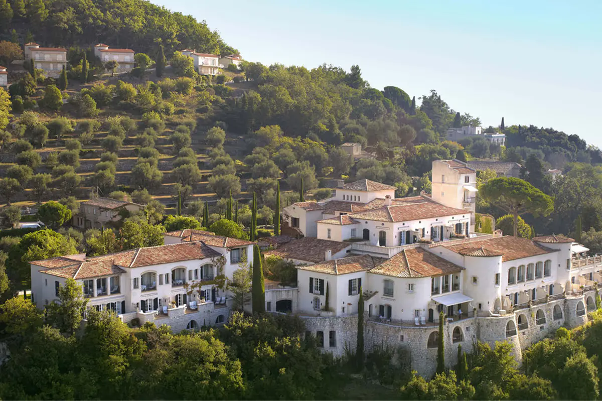 Château buildings on a steep forested hillside with Mediterranean views