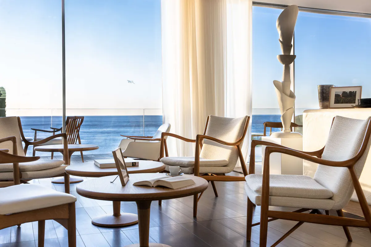 Light-filled lounge with woven chairs and sea views through glass doors