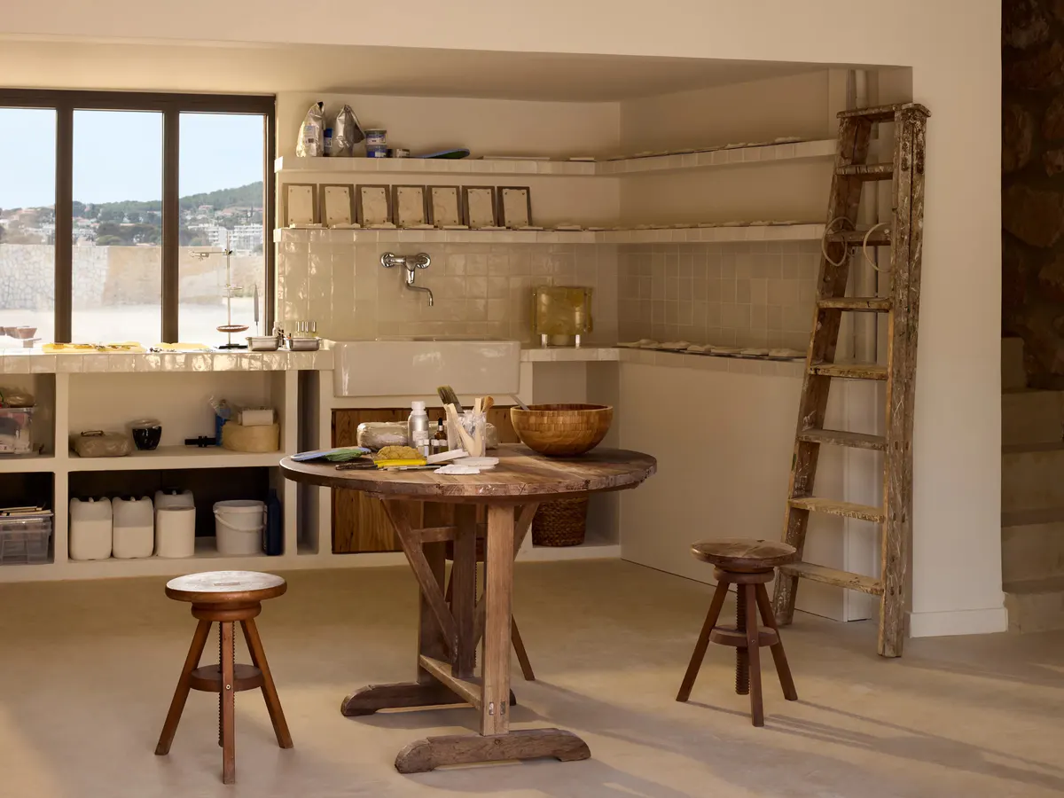 A pottery atelier holds a round worktable, ceramic bowls and a weathered wooden ladder
