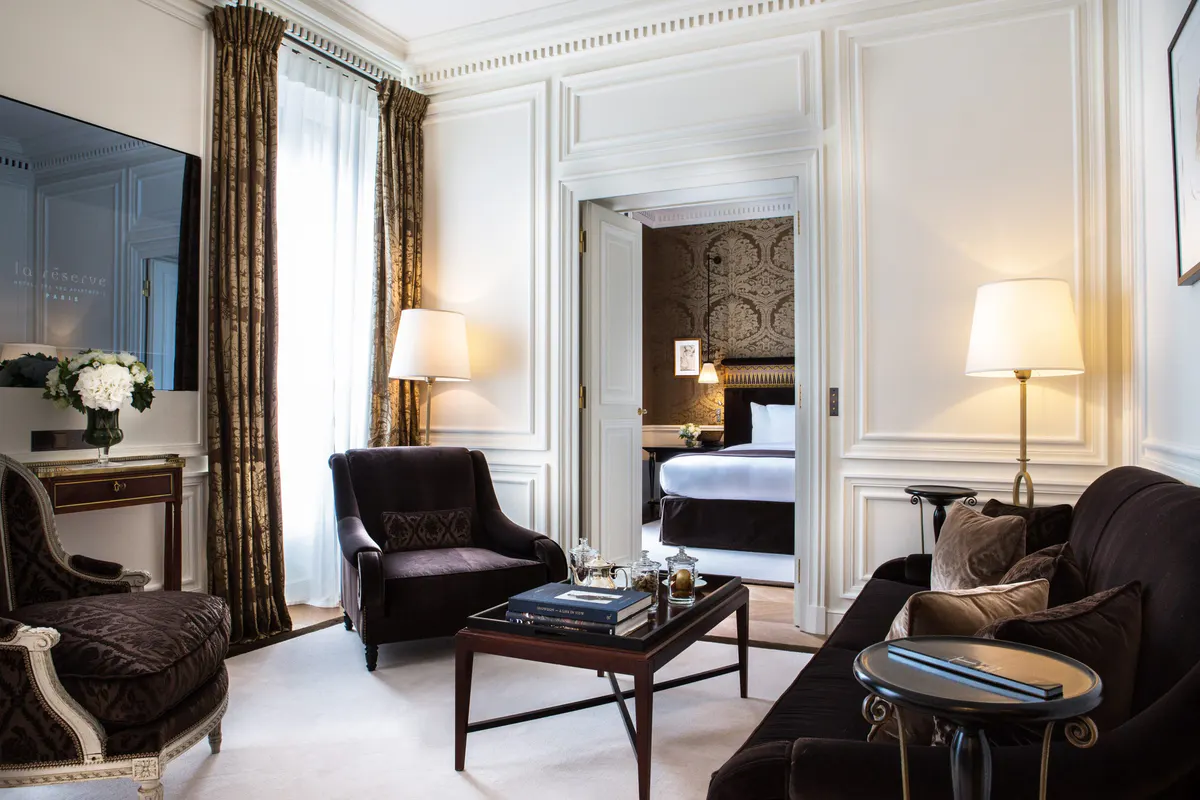 A suite with black velvet armchairs, warm wood furnishings, and layered lighting