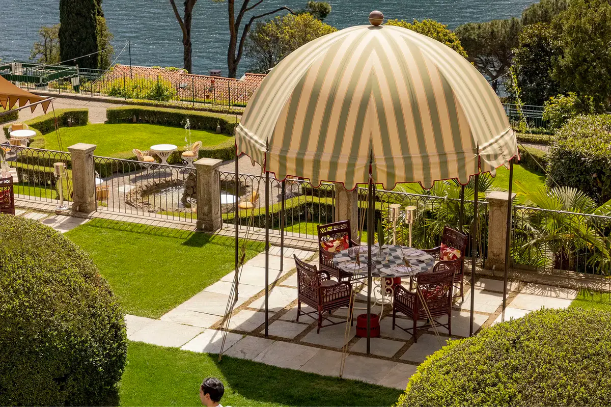 A striped dome tent covers an outdoor dining setup surrounded by manicured hedges