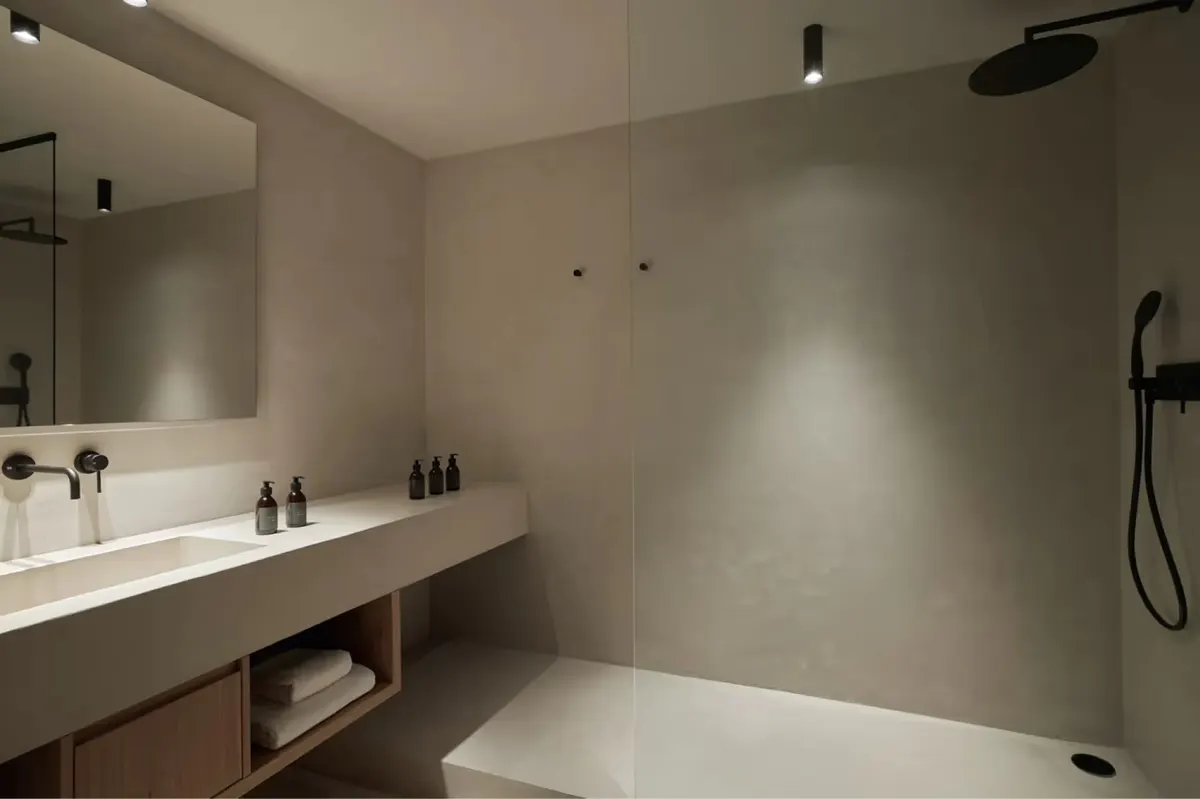 A minimalist bathroom with light walls, a long white vanity, and an open shower area