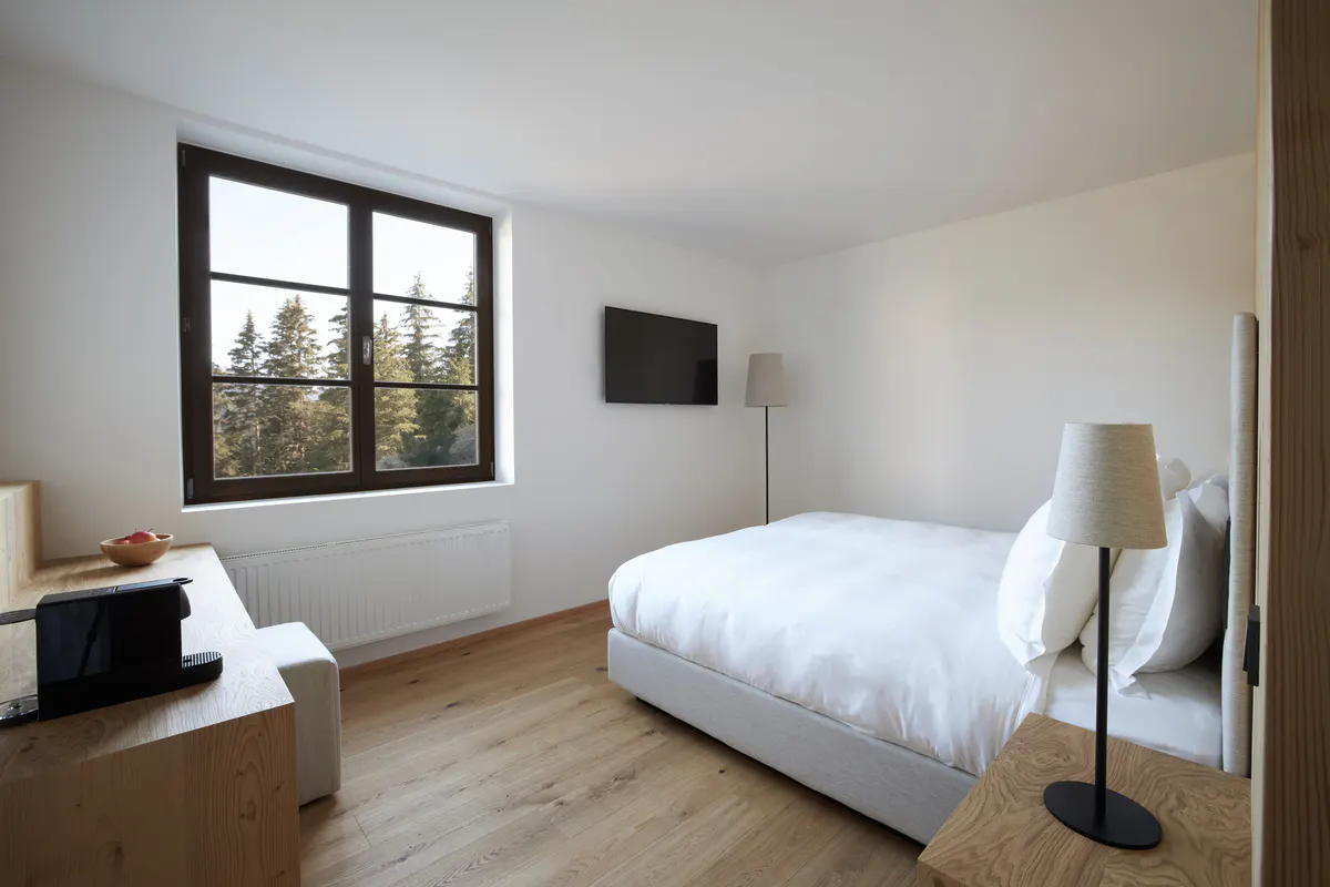 A bright room with a single bed, natural light from a window, and minimal wood and stone furnishings