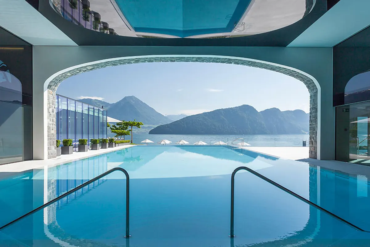 Indoor swimming pool with transparent ceiling and lake vista through large windows