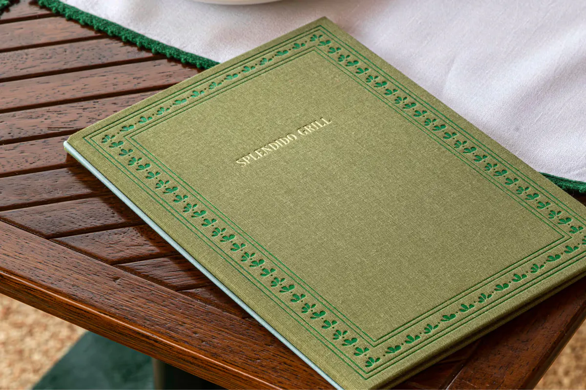 A leather-bound restaurant menu on a wooden table by the sea