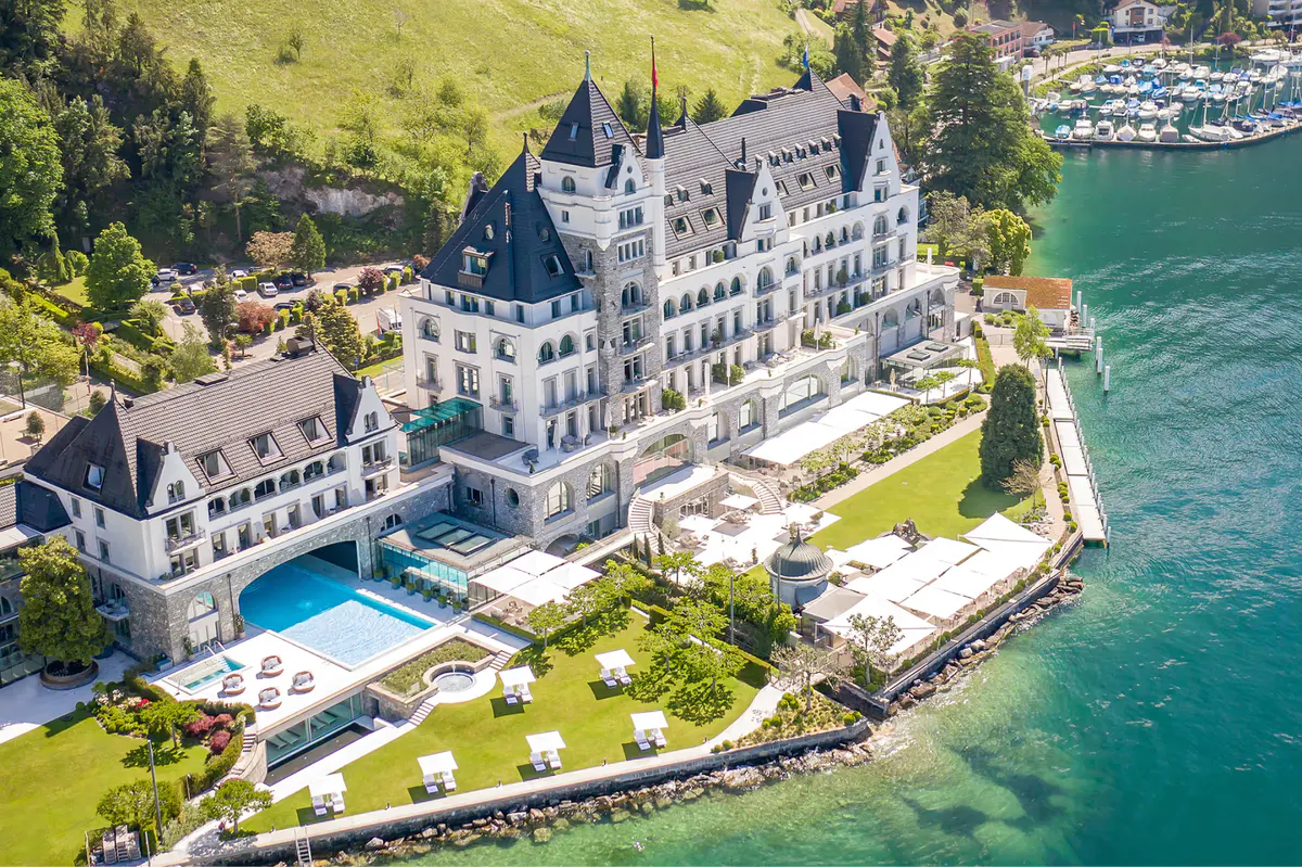 Aerial view of the hotel’s white stone structure on the lake with manicured grounds