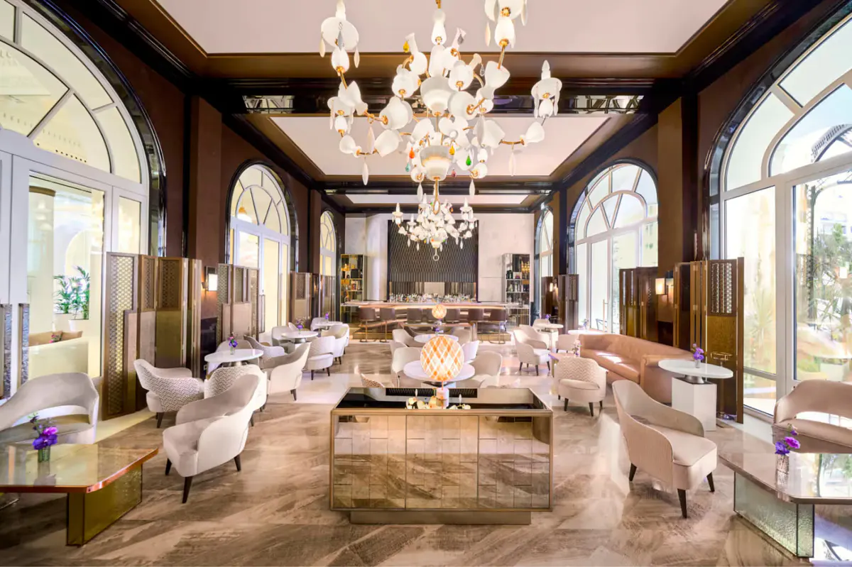 Elegant reception area with dark wood paneling, mirrors, white seating, and crystal chandelier overhead
