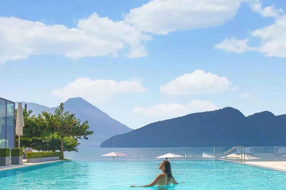 Infinity pool overlooking Alpine peaks and distant lake under blue sky