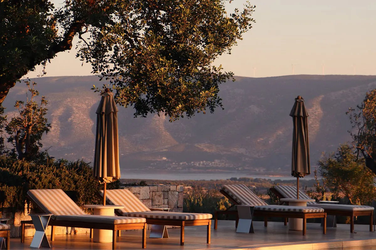 Stone terrace with poolside lounge and distant coastal views