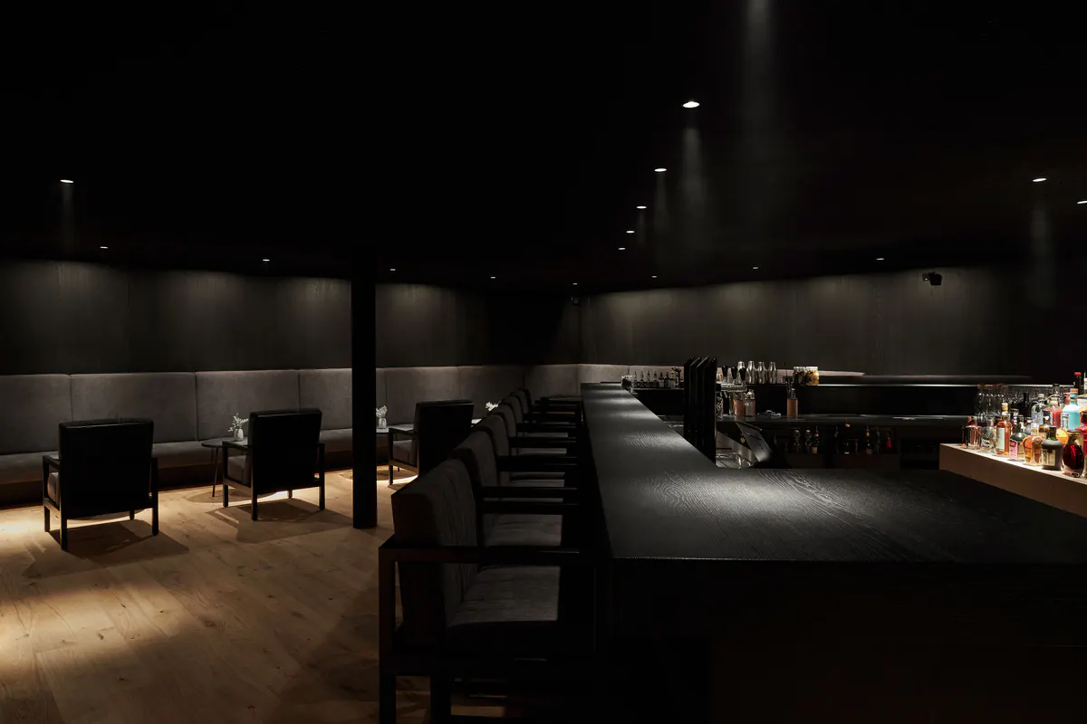 A bar area in cool lighting with dark surfaces and backlighting, stone and modern architectural details