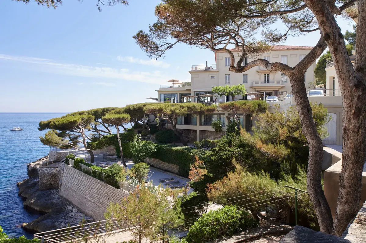 The hotel building on a rocky coastline overlooking the Mediterranean with a pine tree in foreground