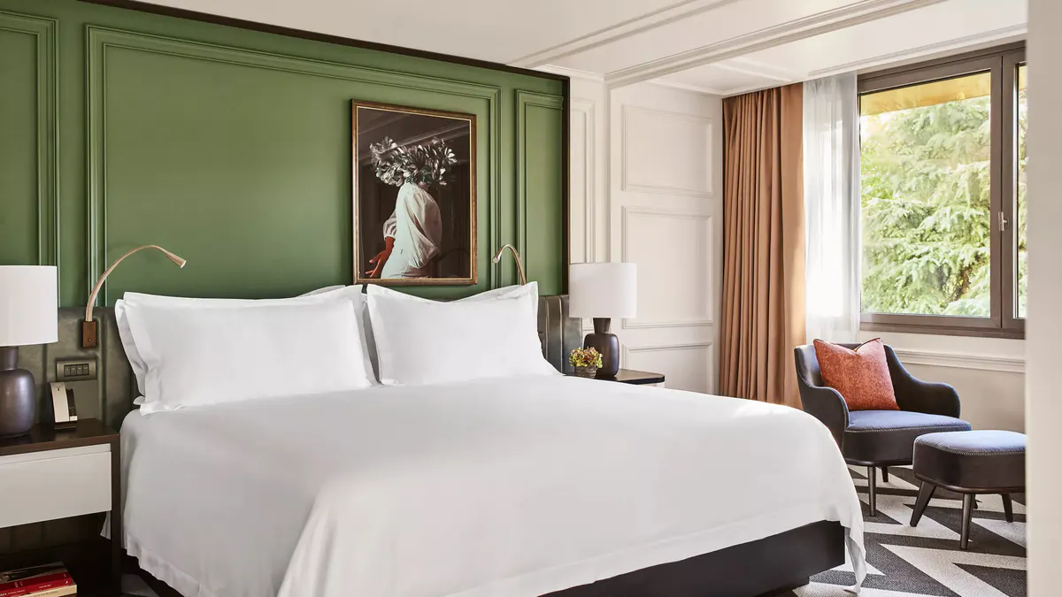 A bedroom with a green accent wall, white linens, and warm wood side tables