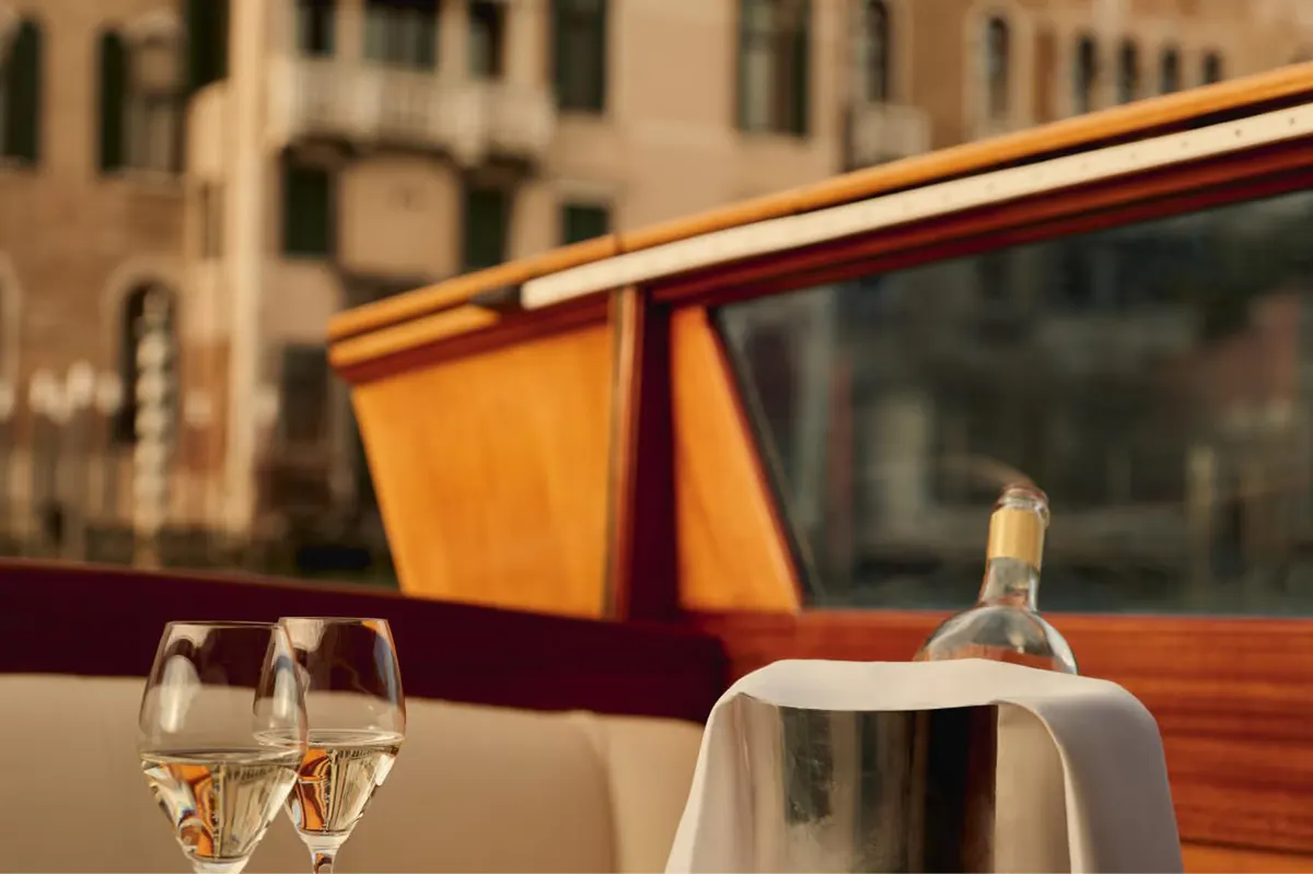 A dining table on a private boat with glasses and the Grand Canal shoreline in the background