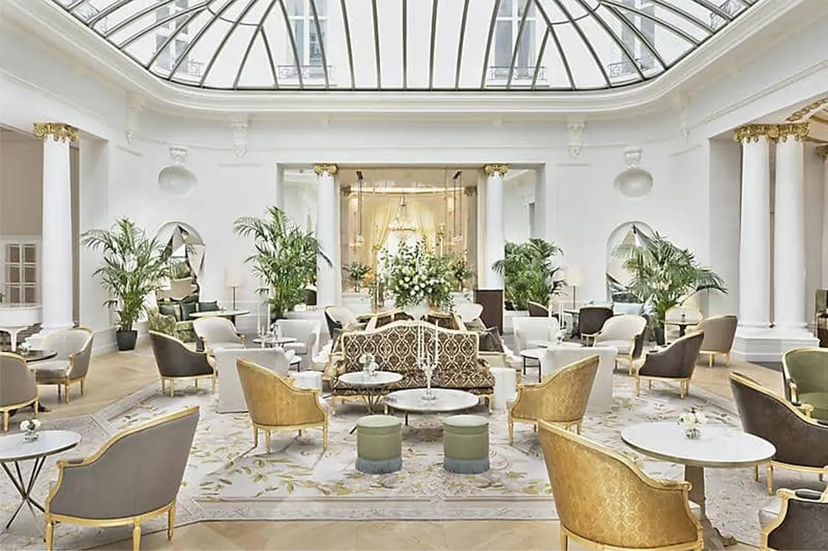 Grand lobby with arched glass ceiling, potted plants, and gold-frame furniture