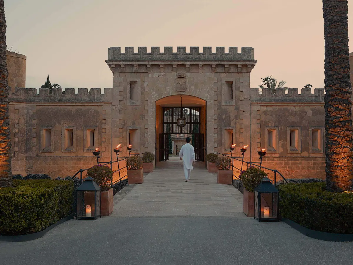 A crenellated fortress gate entrance at sunset, framed by stone archways and lanterns