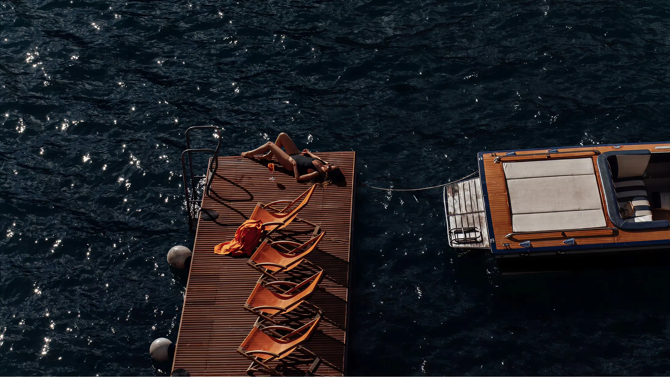 Wooden sunloungers with golden rope detail on a dark water surface
