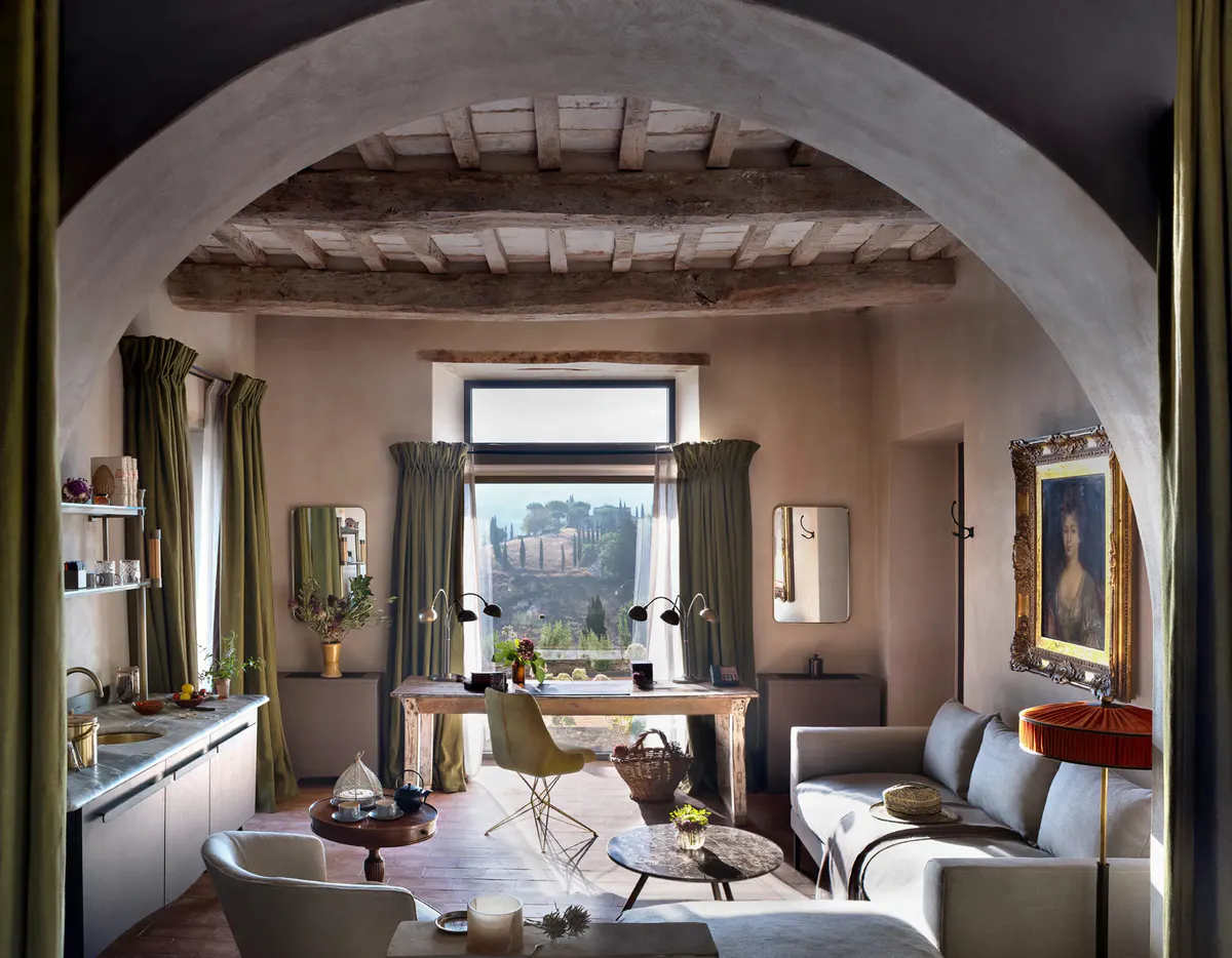 A suite living area framed by a stone archway, with a sofa, dining table, and timber beam ceiling