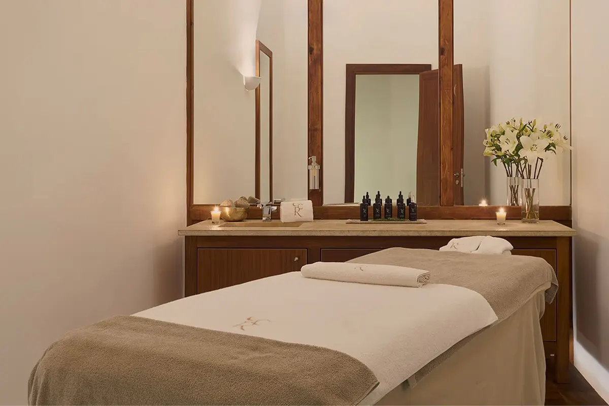 A massage room with a treatment table, mirror, white orchids, and warm natural light