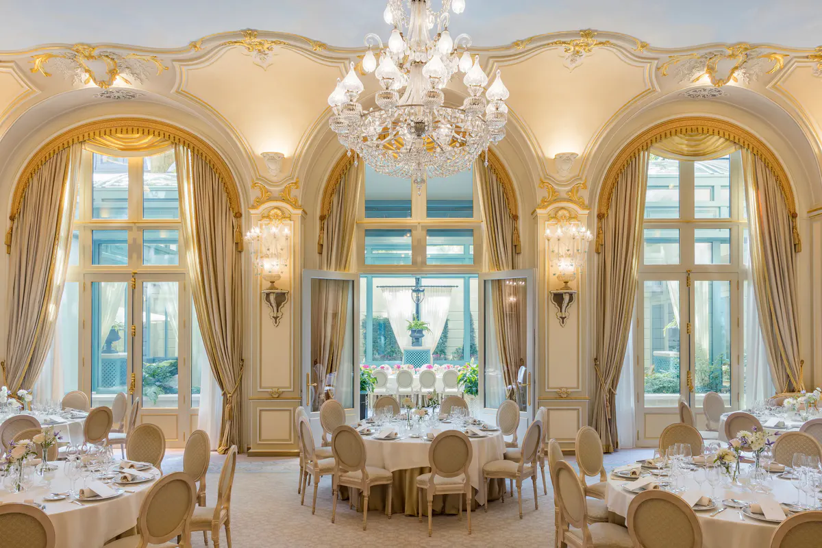 A dining room with gilt arches, crystal chandelier, and tables set for service