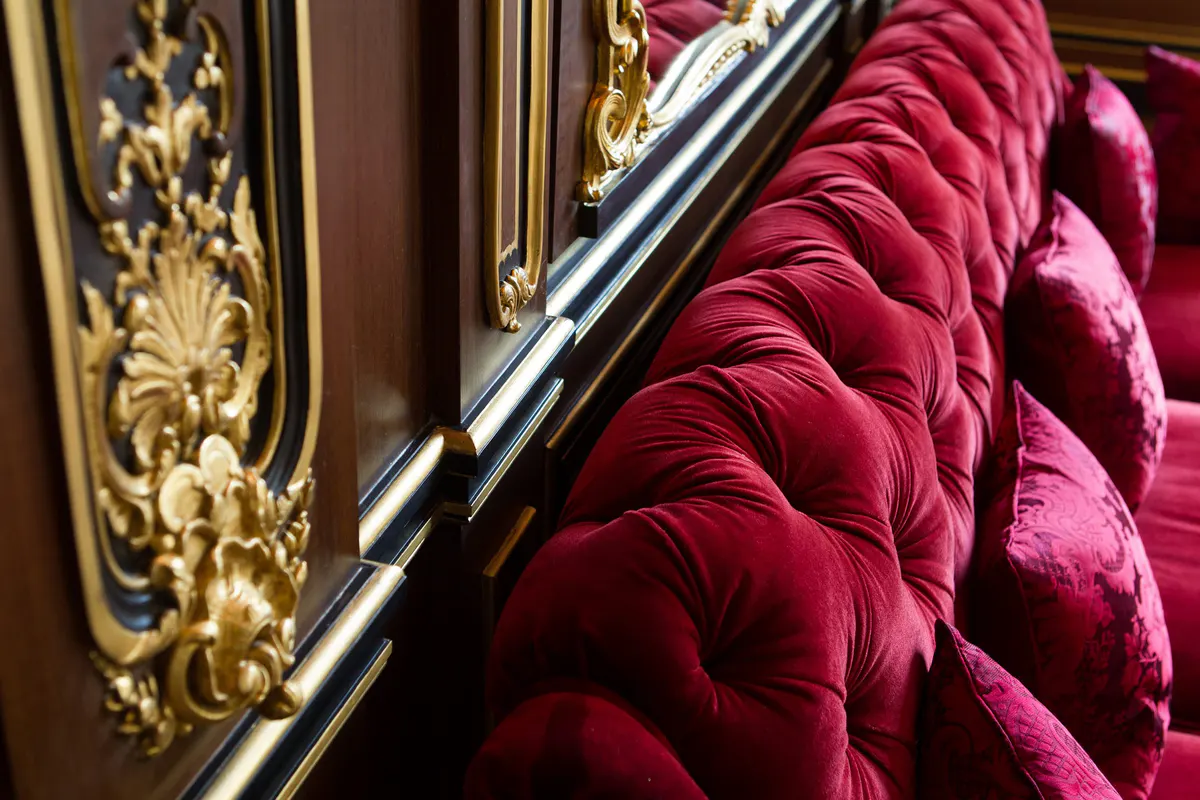 A detail of gold molding with burgundy velvet fabric and polished railings