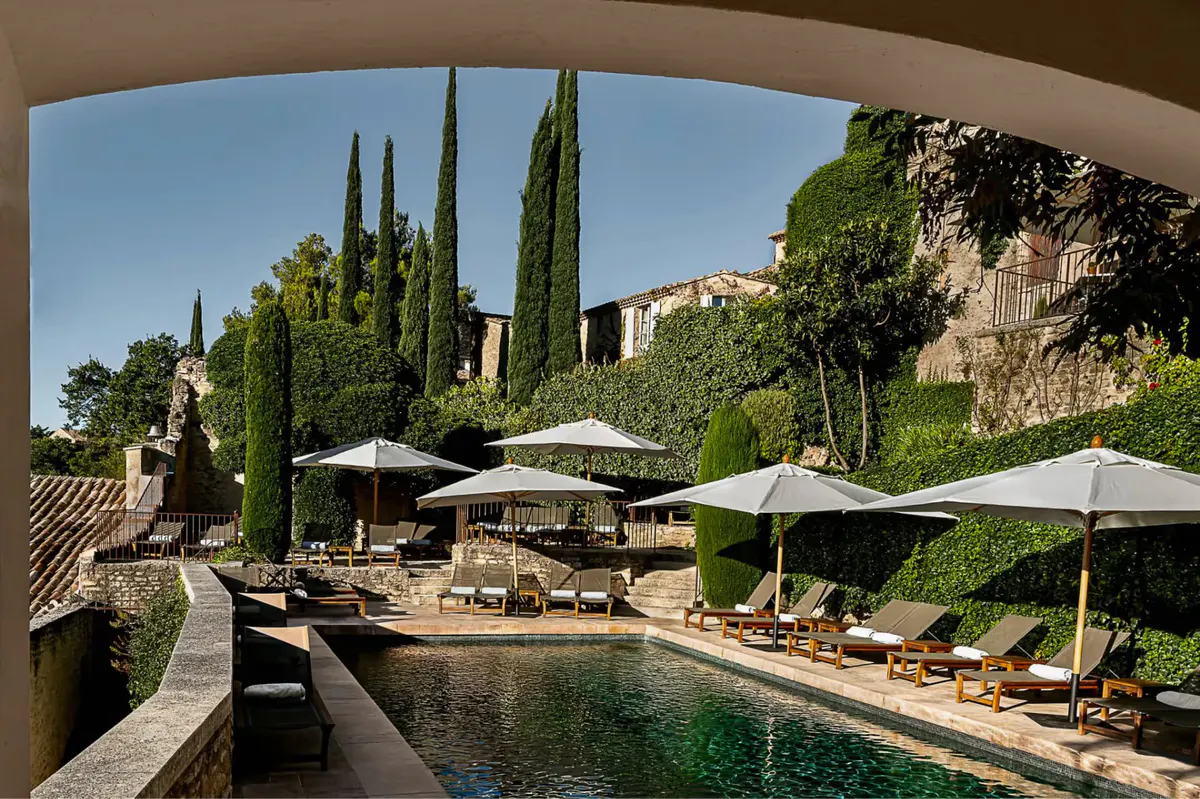A loggia framing the pool terrace, cypress trees, and distant hills under blue sky