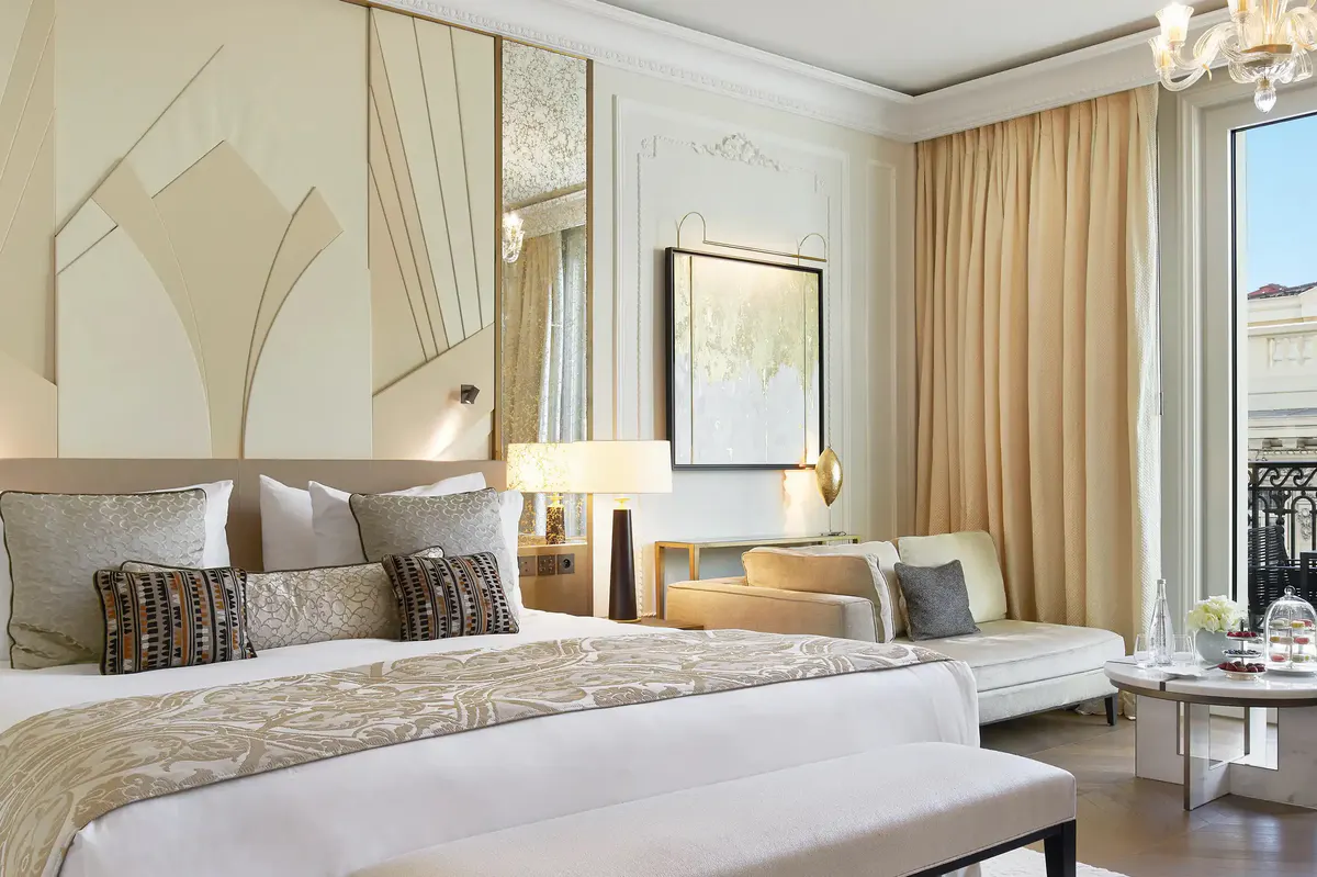 Bedroom with layered neutral bedding and open balcony door to sea view