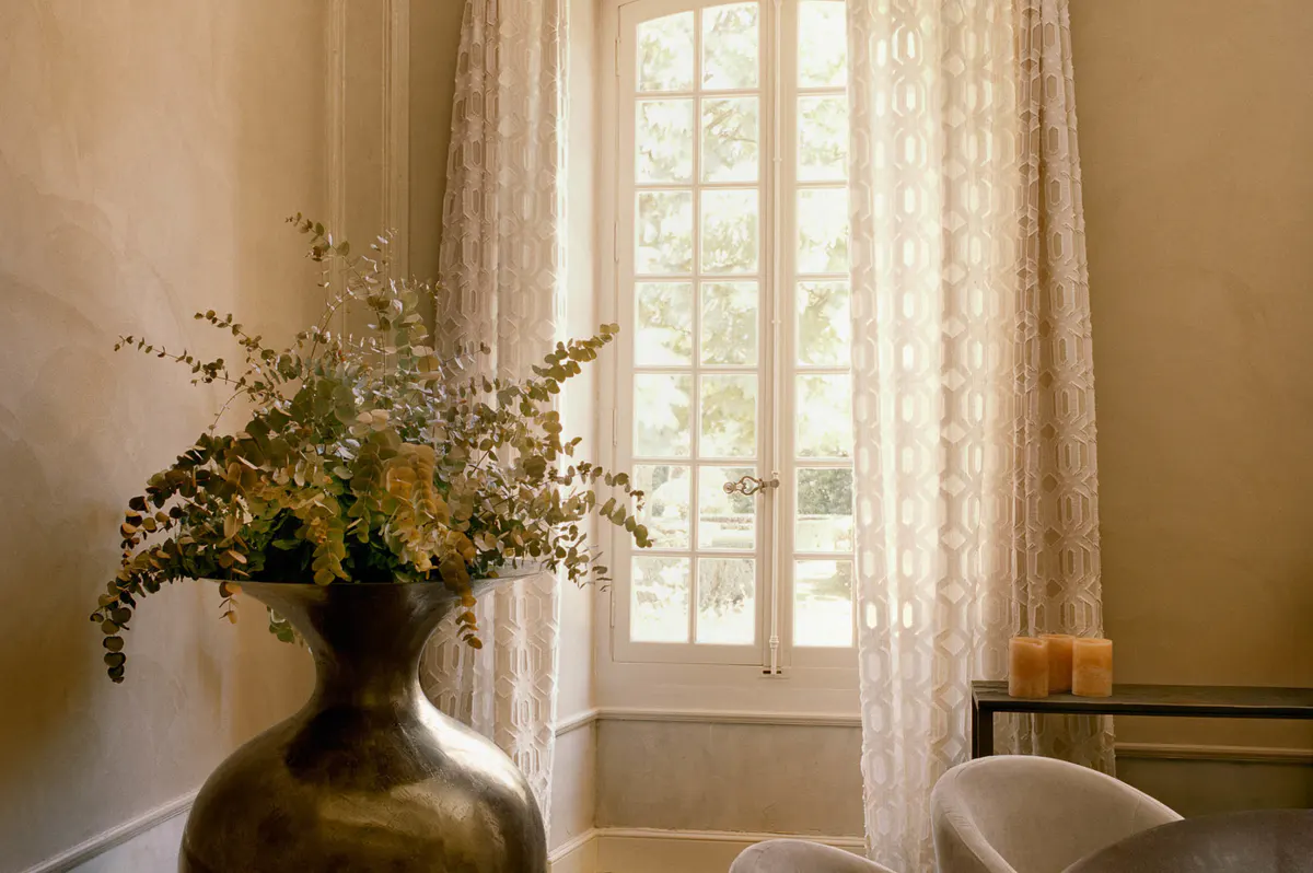Flowers in terracotta vase on windowsill with white gauze curtains and bright daylight