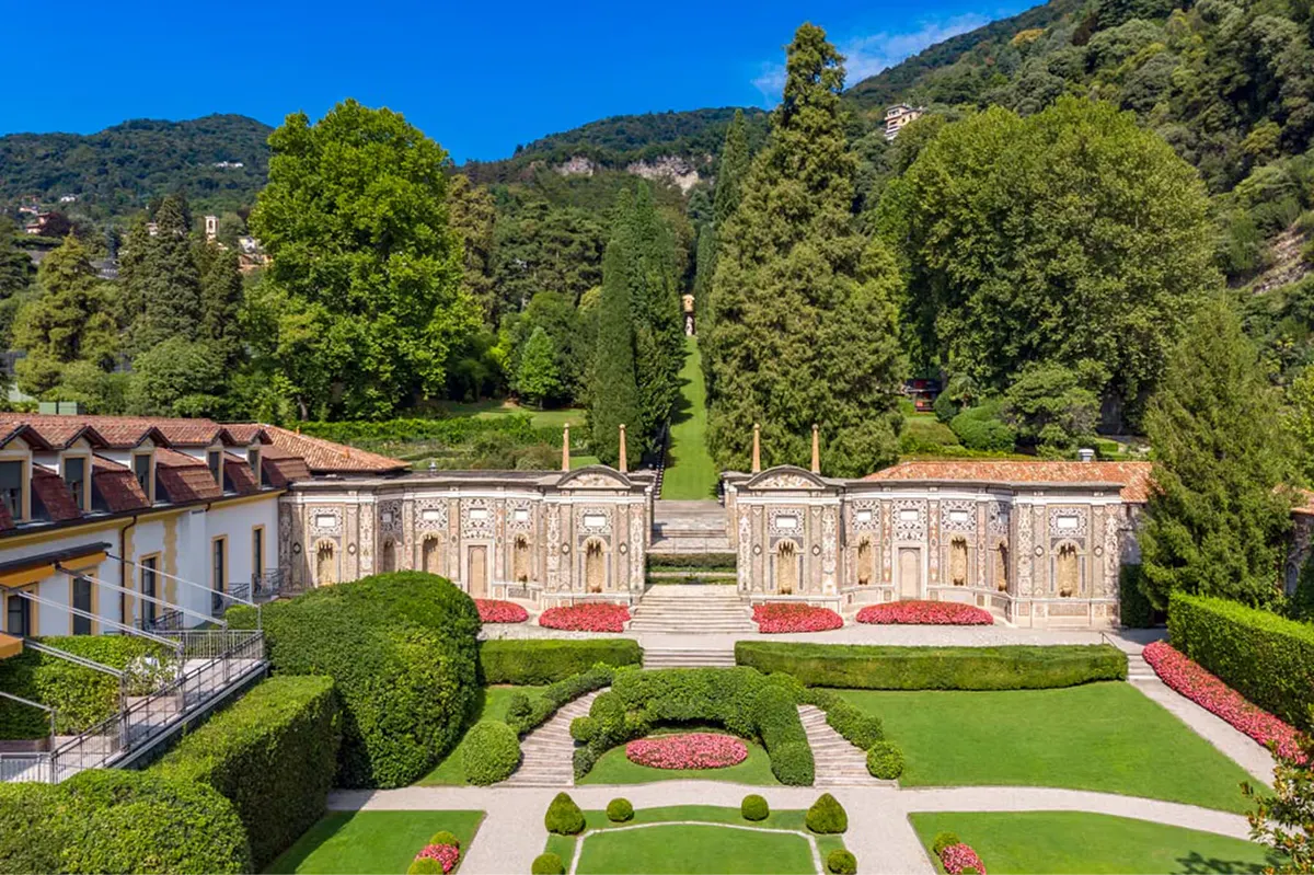 Pink palazzo building on hillside with manicured boxwood hedges and stone statuary