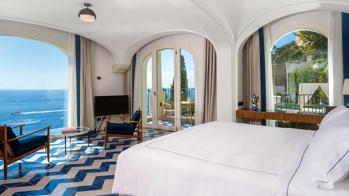 Modern bedroom suite with arched ceilings, sea views through glass doors, and patterned floor