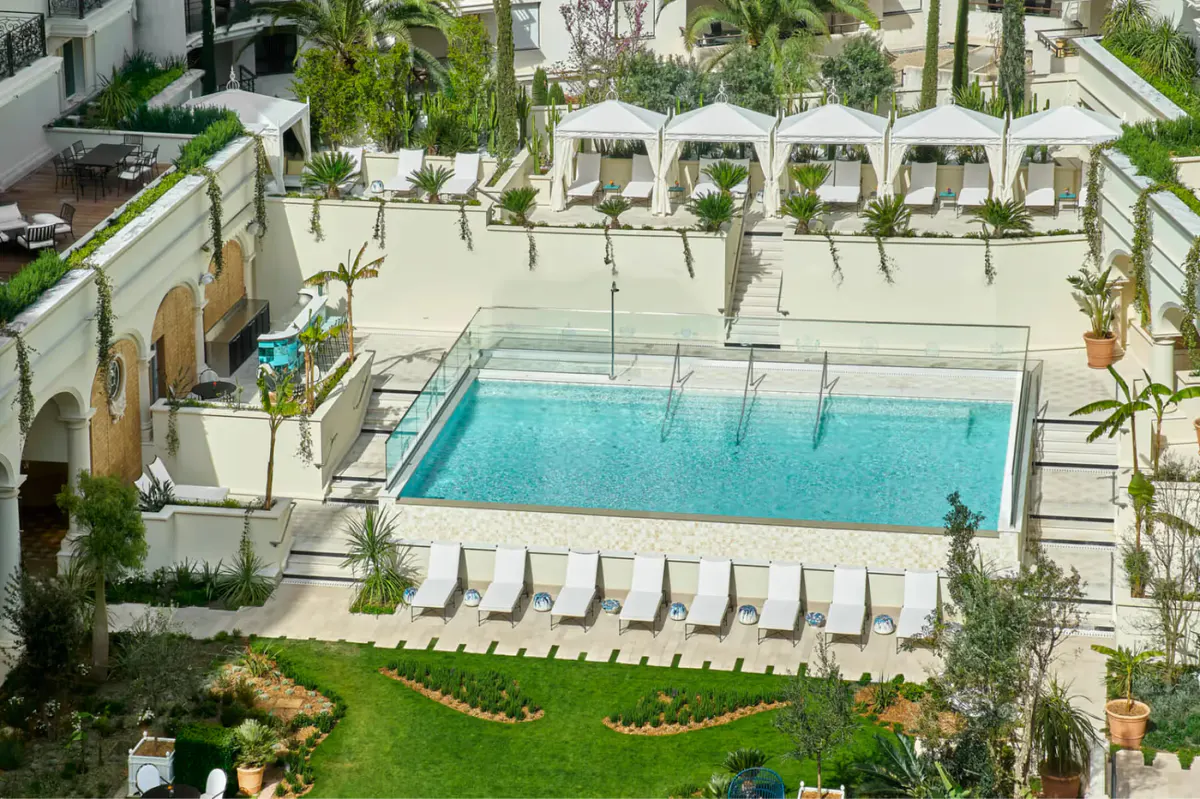 Infinity pool surrounded by white lounge beds and green lawn with hotel building in background