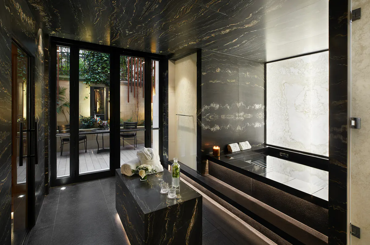 A spa interior with glass doors, dark marble walls, light fixtures, and contemporary furnishings