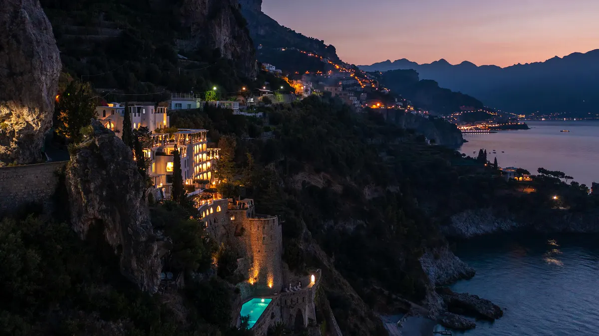 Cliffside property lit at twilight with illuminated terraces cascading down the slope