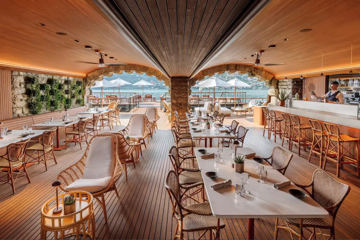 Modern dining pavilion with white linens, wooden furnishings, and panoramic lake views