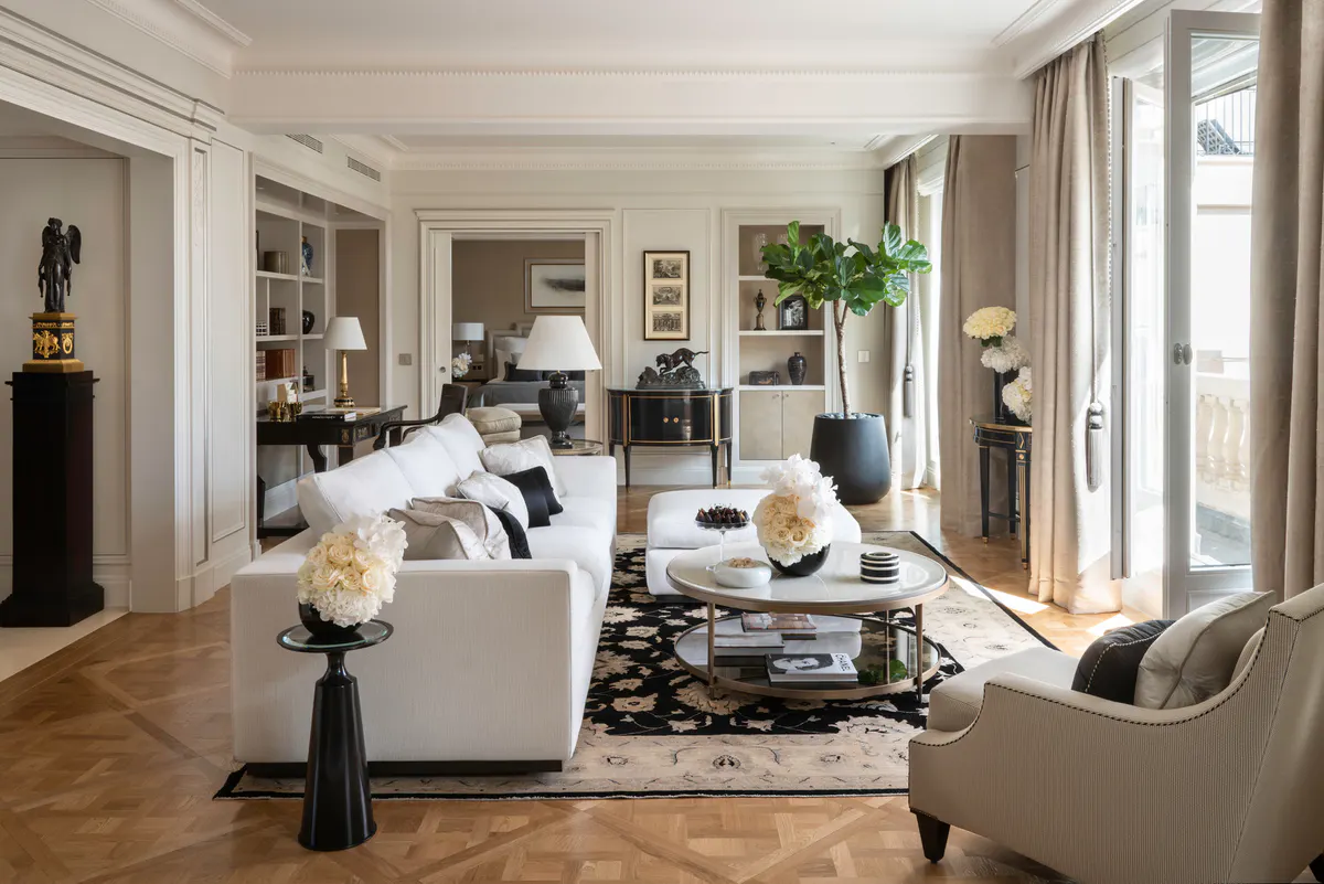 A living area with white armchairs, a black accent cabinet, and sunny windows