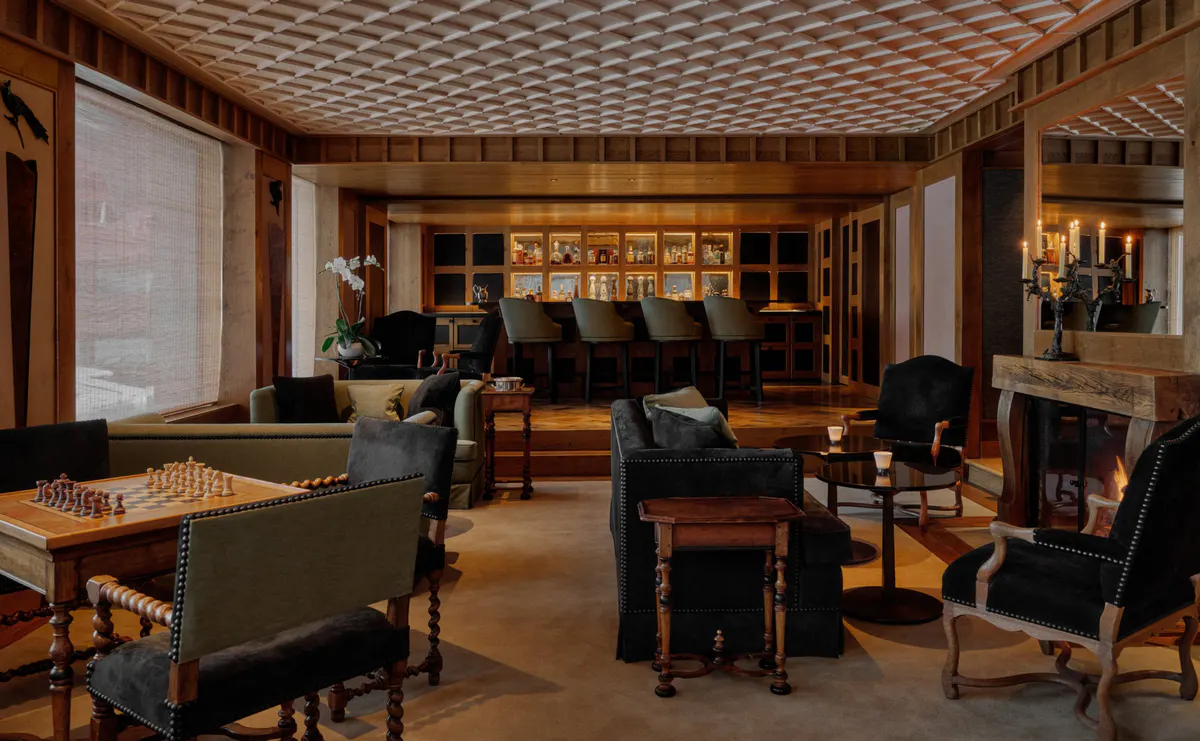 Games room with a fireplace, chess table, leather chairs, and a lit bar beneath a coffered ceiling