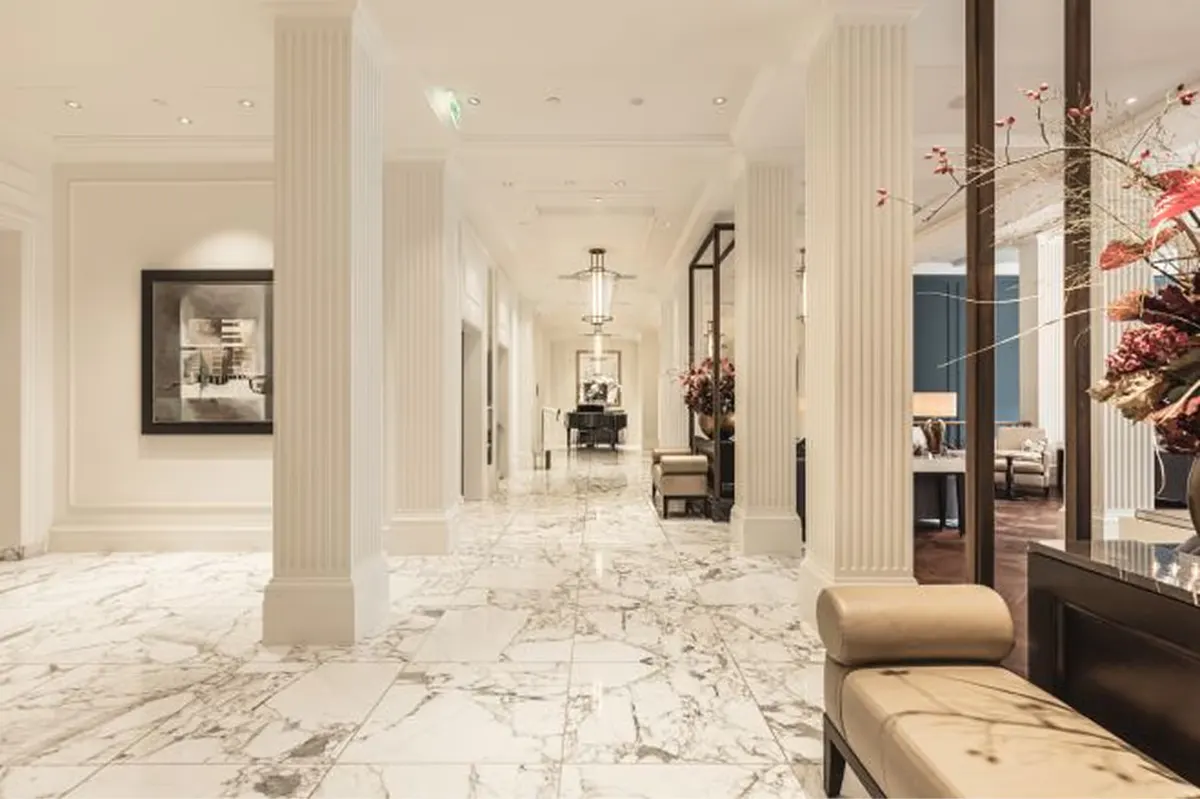 A gallery hallway with marble floors, tall columns, artwork, and cream architectural details