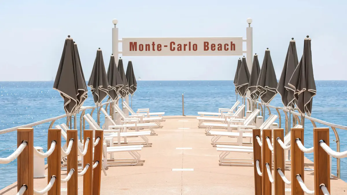 Monte-Carlo Beach with white lounge chairs, charcoal umbrellas, rope railings, and sea views