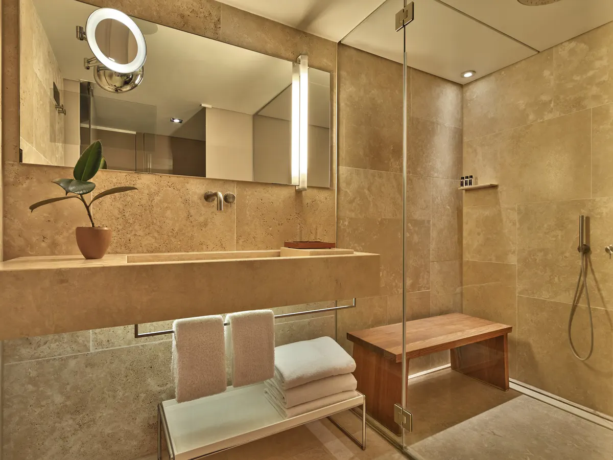 Spa-inspired bathroom with travertine walls, large mirror, and towel warming racks