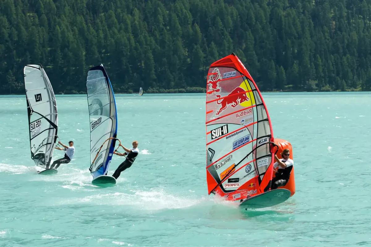 Windsurfing and sailing boards on a turquoise mountain lake framed by peaks