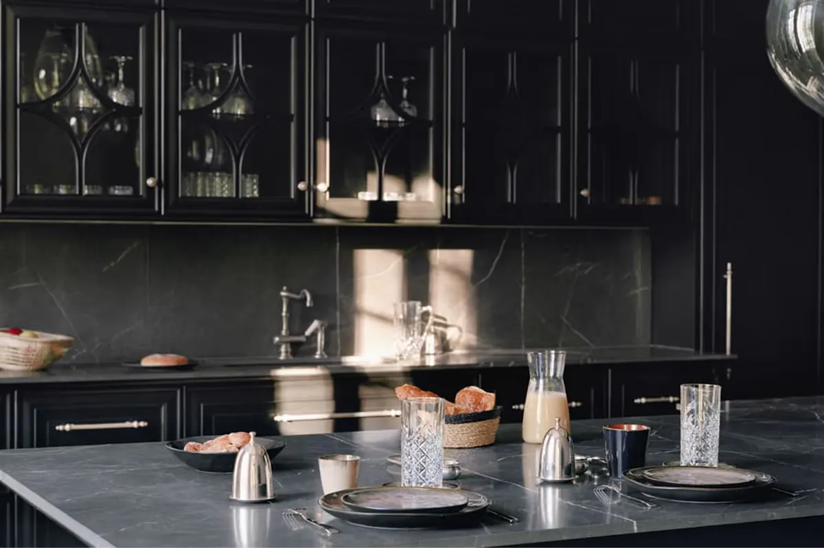 Minimalist black kitchen with dark cabinetry, brass fixtures, and white stone countertop