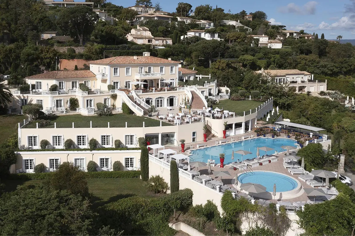 Hilltop villa with white stone facade and swimming pools overlooking forested coastline