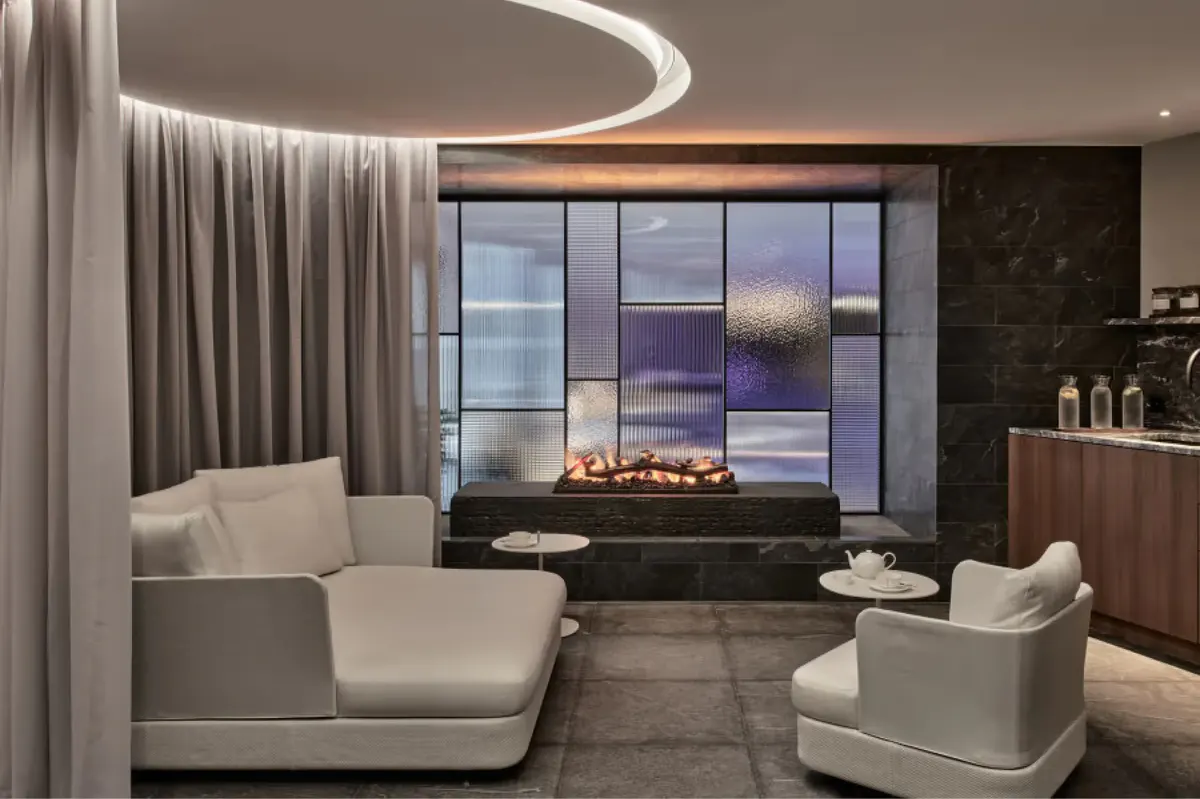 Spa lounge with curved seating, fireplace, and windows overlooking evening mountain scenery