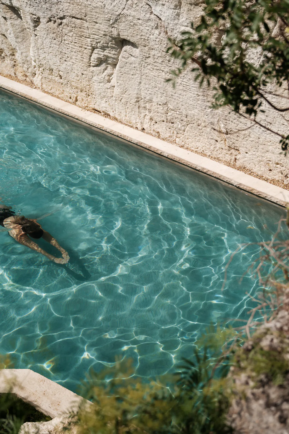 Swimmer in crystal-clear turquoise pool beside textured limestone wall, bright water refraction patterns