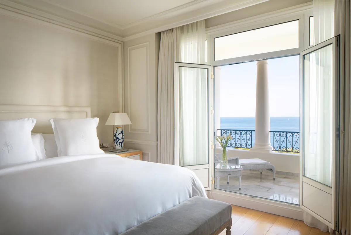 Bright bedroom with white linens and open doors to a sea-view balcony
