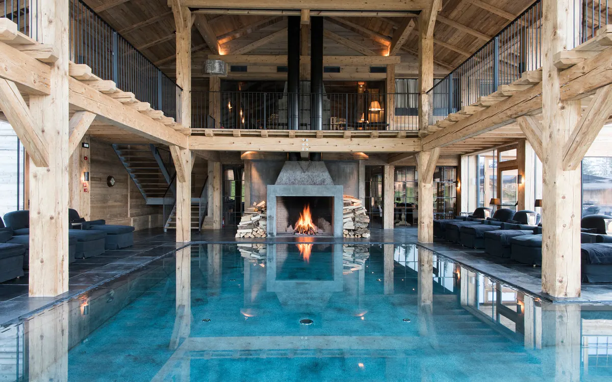 Indoor pool with fireplace, wooden beams, and surrounding windows