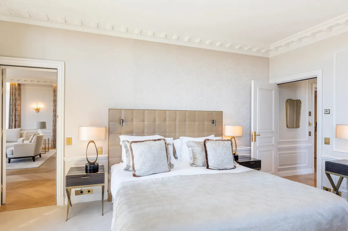 Neutral tone bedroom with beige headboard, paired lamps and sitting area with sea views