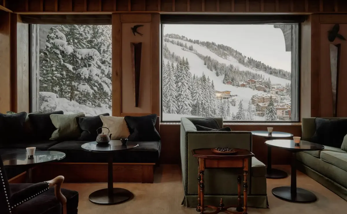 Lounge with deep green sofas, low round tables, and a teapot set before a mountain view window