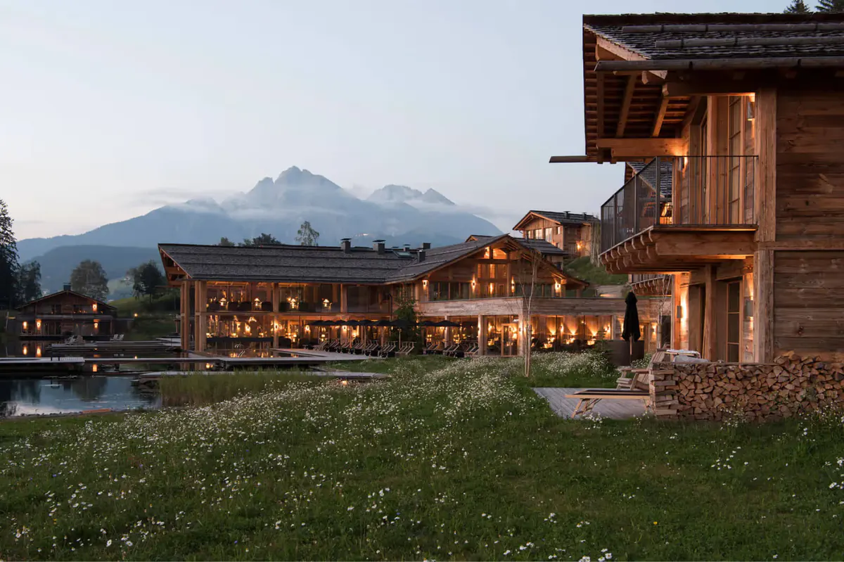 The property at dusk with mountains rising beyond lit wooden structures